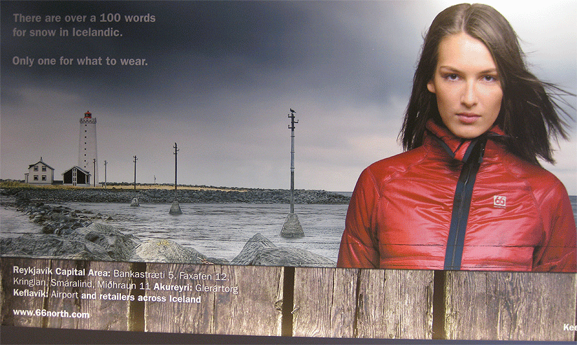An advertisement for “66 North.” The image has three photographic elements and two typographic elements: the top two thirds of the image presents, in the foreground, a young woman wearing a winter jacket with a “66 North” logo, and, in the background, a scene which includes a waterway, rocks, land, and a lighthouse; the bottom third of the image is a wooden fence. Text in the upper segment reads: “There are over 100 words for snow in Icelandic. Only one for what to wear.” Text in lower segment details business locations and www.66north.com.